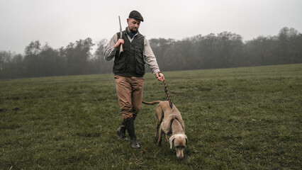 Hunter man with dog in traditional shooting clothes on field holding shotgun.