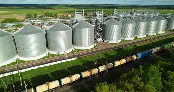 A freight train passes grain storage tanks. Aerial view of train and grain elevator.