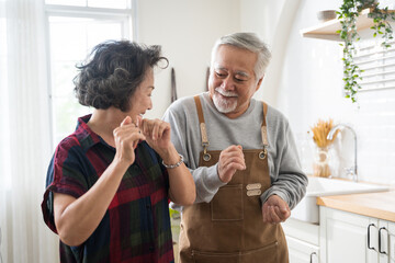 Asian mature senior couple is dancing and smiling in kitchen at home. - Powered by Adobe