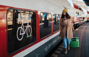 Happy young traveler woman with luggage boarding in the train at train station platform