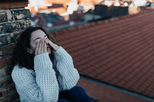 Unhappy young woman resting and sitting on the roof with city view.