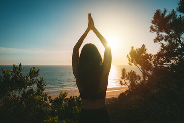 Silhouette of young healthy woman practicing yoga with ocean view at sunset. Rear view of woman...