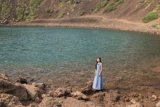 Girl in long blue dress standing in crater of volcano in Iceland