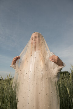 portrait of blonde girl in the field wearing white dress and veil
