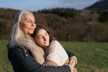 Happy senior grandmother with teenage granddaguhter hugging in nature on spring day.