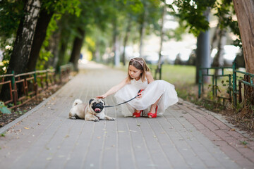 European girl child in white dress in red mother's shoes with heels on walk with pug, joyful child in summer with pet