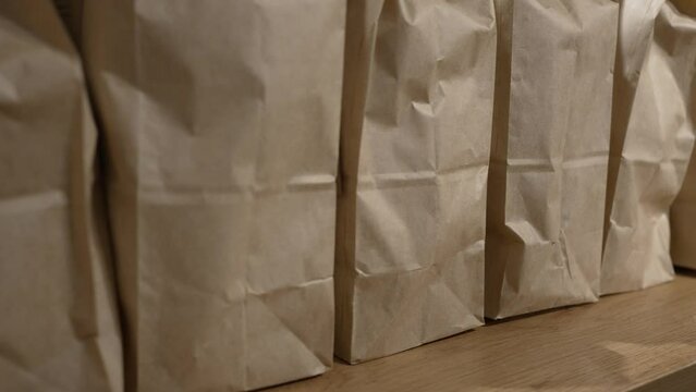 Row of paper bags with products stand on wooden table in bakery shop. Paper bags with guest orders on wooden table in cafe closeup