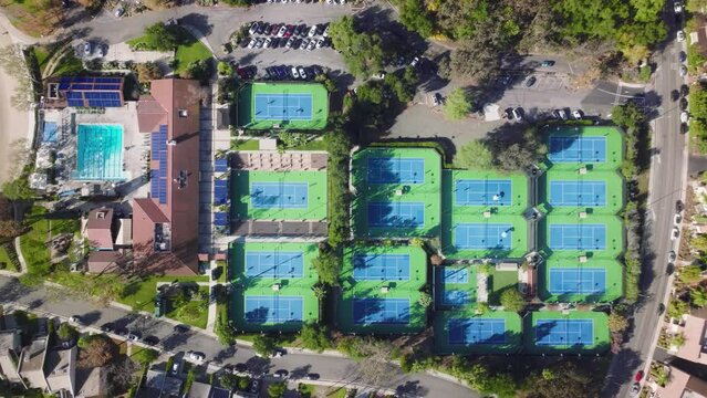 High angle top down still aerial drone shot above people playing tennis on many tennis courts in the fitness club with pool in park area. Calabasas recreation center at expensive real estate houses