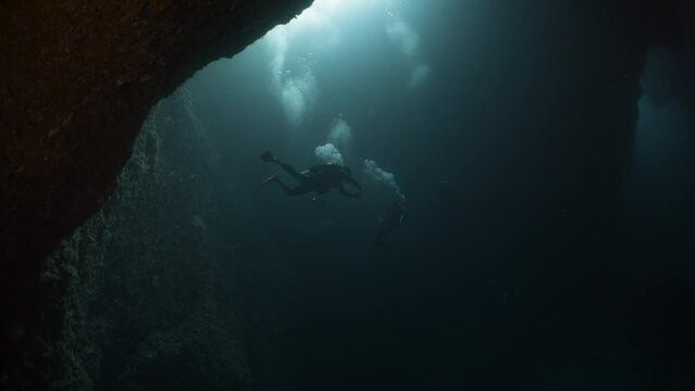 Scuba divers explore dark underwater cave