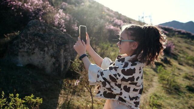 Happy girl takes a selfie on a mobile phone in a flowering garden of mountain wild rosemary at sunset