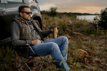 Naklejka na ściany i meble Young man is drinking tea while fishing. Outdoor picnic concept