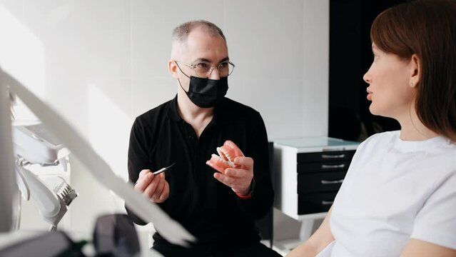 Dentist and patient discuss treatment plan using dental models. Young woman talking to orthodontist about braces treatment during consultation