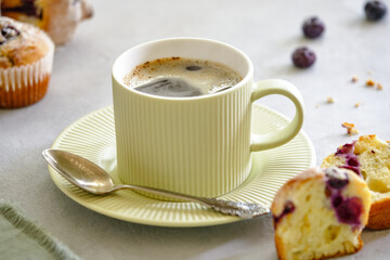 A cup of hot black coffee with fragrant lemon muffins with blueberries on a gray background