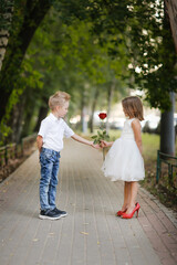 Naklejka na ściany i meble cute couple of children boy and girl, boy gives his girlfriend rose for walk in summer. Girl child in high heels, children play dating and courtship, relationship and growing up concept