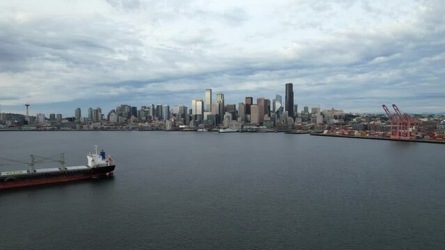 Seattle, Washington skyline with moody sky. Aerial drone footage flying over harbor past a cargo ship.