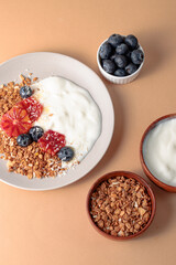 breakfast table with granola bowl with greek yogurt decorated by blood oranges, blueberry and coconut. beige background. ingredient for breakfast. top view