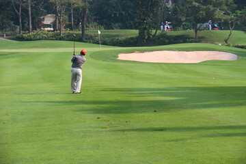Obraz premium An unindentified Asian golfer hitting a ball near bunker on golf field. 