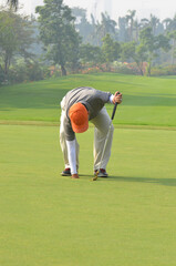 Unidentified Asian man picking up golf ball from a golf hole.