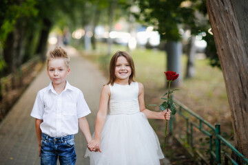 kids play dating and courtship, cute couple of children boy and girl, boy gives his girlfriend rose for walk in summer. Girl child in high heels, relationship and growing up concept