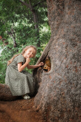 Portrait of adorable little kid girl near the tree with squirrel on it in forest