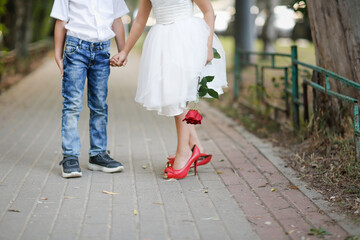 Obraz premium cute couple of children boy and girl with rose on walk in summer. Girl child in high heels, children play dating and courtship, relationship and growing up concept