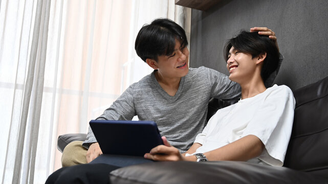 Loving young gay couple using digital tablet together in living room. Concept of sexual freedom and equal rights for LGBT community