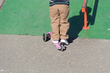 Obraz premium A little boy in brown pants and a cap is having fun and diligently studying extreme sports, riding a scooter in summer on the playground, in the park and outdoors.