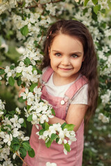 A little girl smiles next to a flowering tree.
