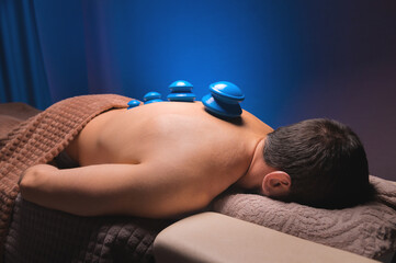 Close-up of a man's back with rubber vacuum cans installed in a dark room of a spa salon