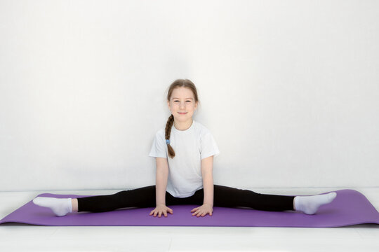 cute little girl sits on a leg-split stretching her little toes and smiling