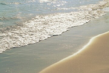 Ola suave con su espuma sobre la dorada arena del mar Mediterráneo. Ola en la playa del Cabanyal en la ciudad de Valencia, España. - obrazy, fototapety, plakaty