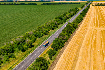 trucks driving on asphalt road along the green fields whith rolls of haystacks. seen from the air....