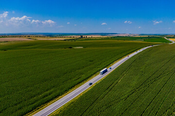 blue truck driving on asphalt road along the green fields. beautiful clouds in the blue sky. Aerial...