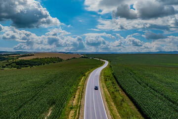 Fototapeta na wymiar car driving on asphalt road along the green fields. beautiful clouds in the sky. Aerial view landscape. drone photography. transportation and travel concept.