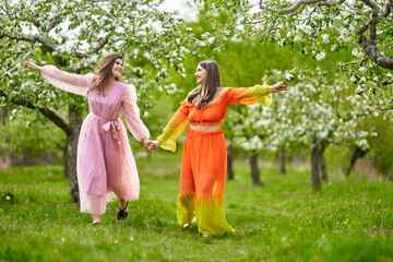 Naklejka na ściany i meble Two women of mixed race walking hand in hand through an orchard