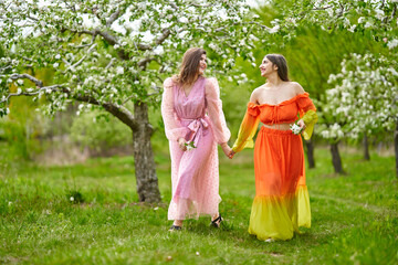 Naklejka na ściany i meble Two women of mixed race walking hand in hand through an orchard