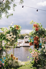 Arch design for the wedding ceremony is decorated with flower arrangements and stands on the lake background and Yacht Club