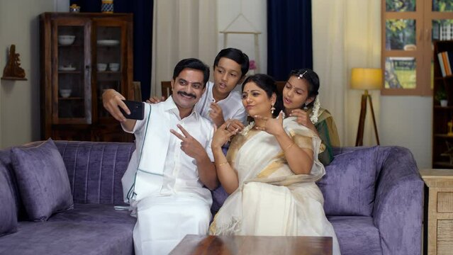 An attractive South Indian couple and their young kids taking a selfie together - a modern lifestyle  photogenic. A cheerful South Indian family having fun together in the living room - a fun activ...