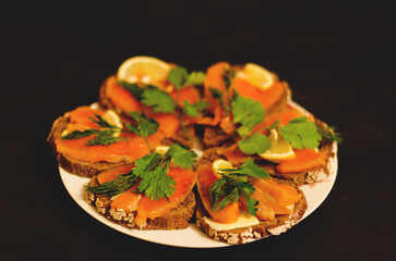 Sandwiches, canape with smoked salmon, butter, herbs on the festive table. Top view food. Black background. Healthy lifestyle, diet