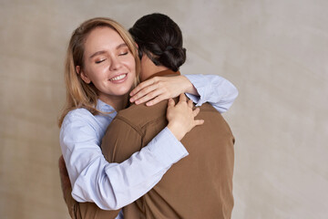 Horizontal medium portrait shot of happy blond woman in love embracing her boyfriend with her eyes closed