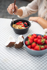 Girl eating granola with strawberries and coconut in nature. Breakfast pellet at the campsite. Healthy eating and a tasty snack. 