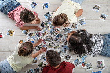 Top view of family with children lying on the floor surrounded by memories on printed photographs...