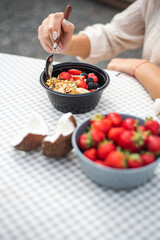 Girl eating granola with strawberries and coconut in nature. Breakfast pellet at the campsite. Healthy eating and a tasty snack. 