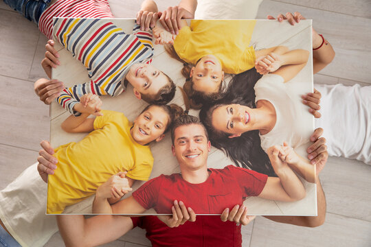 Family holds the same picture of themselves while lying on the floor, smiling
