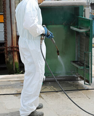 worker of the pest control company with protective suit while cleaning the street furniture with a...