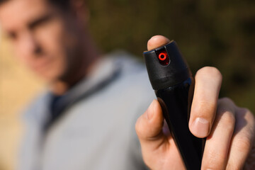 Man using pepper spray outdoors, focus on hand. Space for text