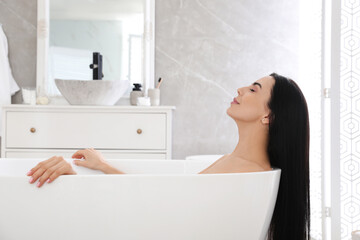 Beautiful young woman relaxing in bathtub at home