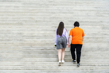 The guy and the girl with excess weight climbs the concrete stairs. Back view. unrecognizable person