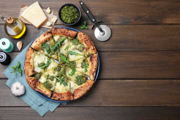 Delicious pizza with pesto, cheese and arugula served on wooden table, flat lay. Space for text