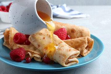 Pouring honey onto delicious crepes served with berries on light grey table, closeup